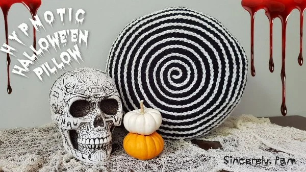 A black and white spiral crochet pillow with a skull and pumpkins.