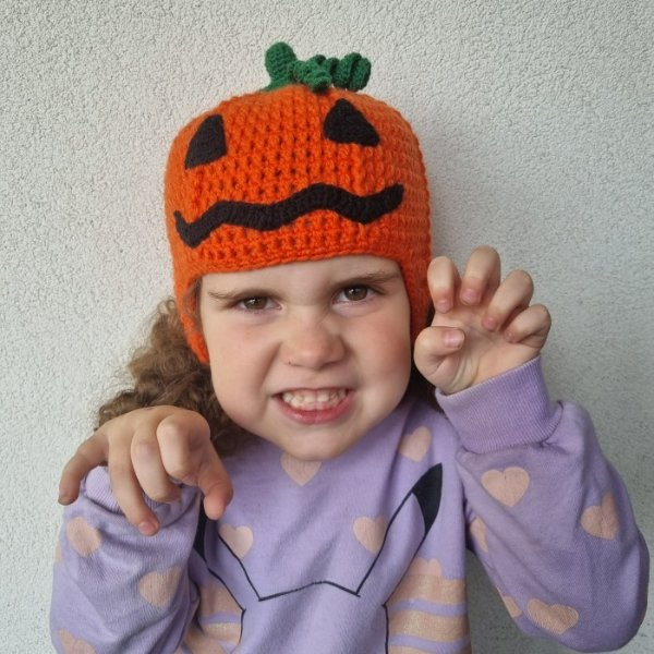 A child wearing a crochet jack o lantern hat.