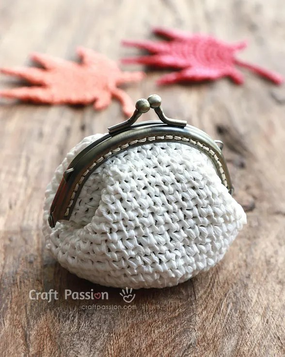 A white crochet coin purse with a kisslock clasp o a wooden background.