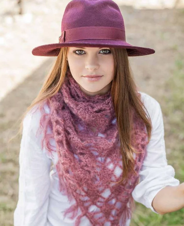 A woman wearing a fuschia coloured lacycrochet scarf and a matching hat.