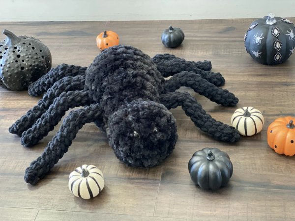 A big furry crochet spider surrounded by miniature pumpkins.