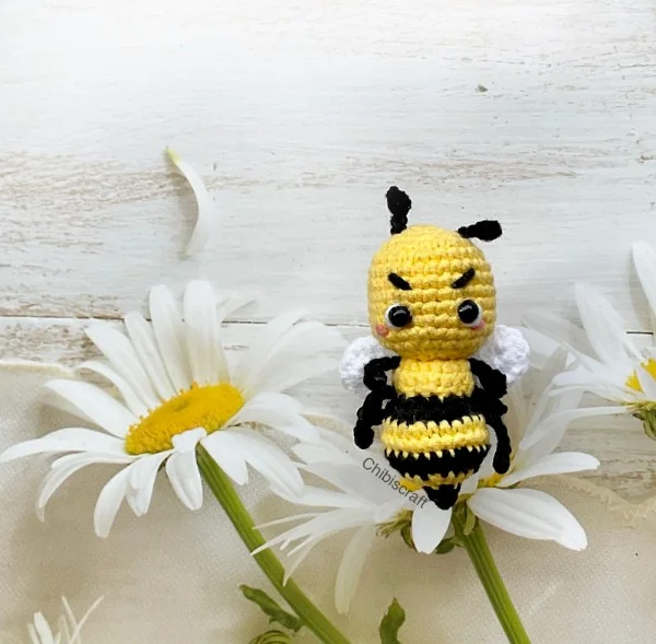 A small amigurumi crochet bee lying on his back with white daisies.