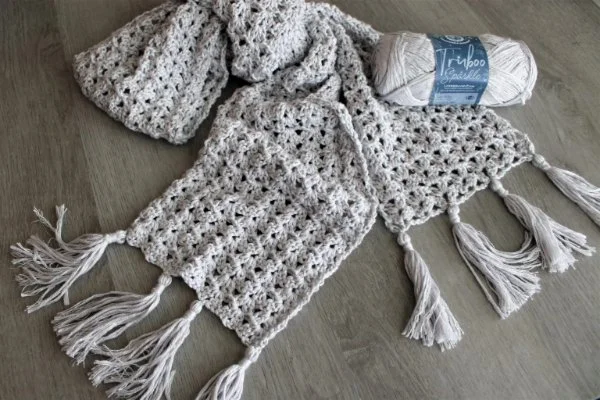 A light coloured, crochet lace scarf with tassels.