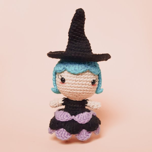 A crochet withc with blue hair and a purple and black dress.