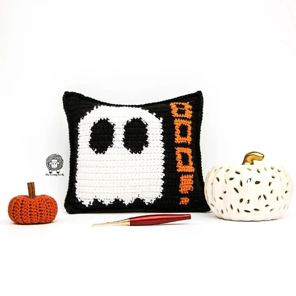 A crochet ghost pillow with a crochet pumpkin in the foreground.