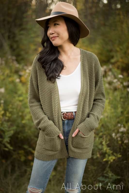 A woman wearing an olive green coloured crochet cardigan with pockets.