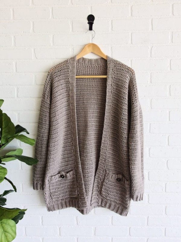 A crochet cardigan with pockets on a wooden hanger.