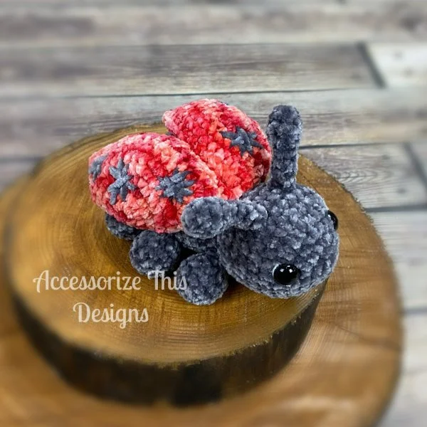 An amigirumi crochet ladybug on a small round of timber.