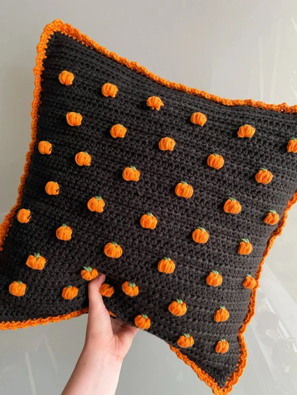 A black crochet pillow with little halloween pumpkins.