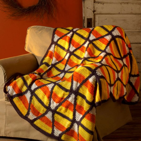 A candy corn themed crochet blanket draped over a sofa.