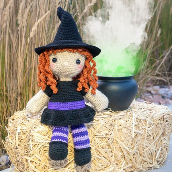 A crochet witch doll with curly orange hair and striped purple stockings.