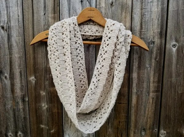 A white crochet lace scarf on a wooden coat hanger with a timber paling fence in the background.