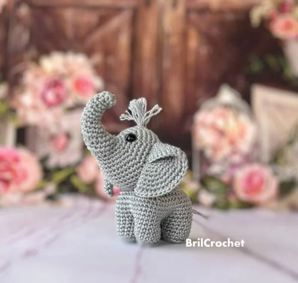 A mini crochet elephant with pink flowers in the background.