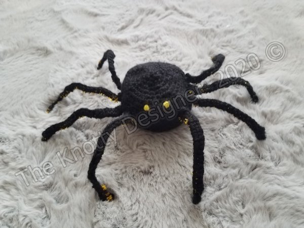 A black crochet spider with long legs and neon yellow eyes.