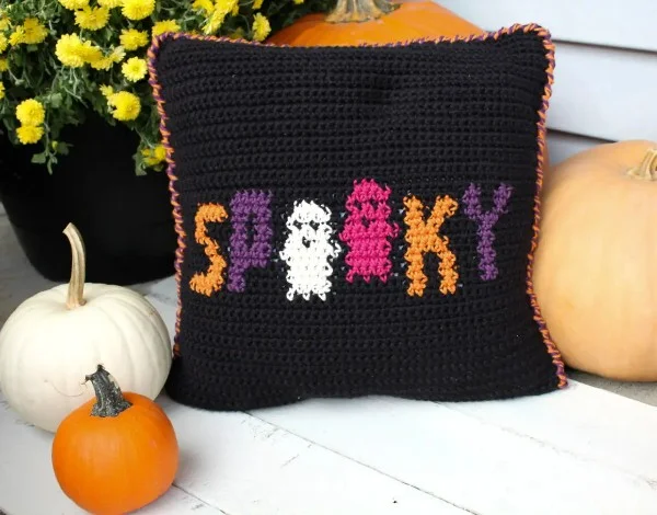 A black crochet pillow with the word spooky on the front with two ghosts.