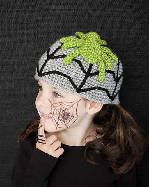 A child qearing a Halloween-themed crochet hat with a spider web and spider.