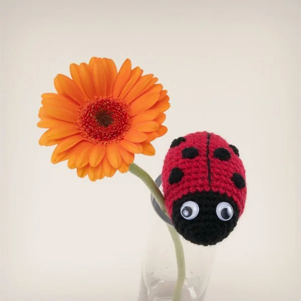 A crochet ladybug on a flower vase.