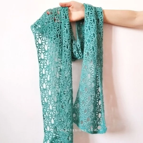 A delciate blue crochet lace scarf with a white background.