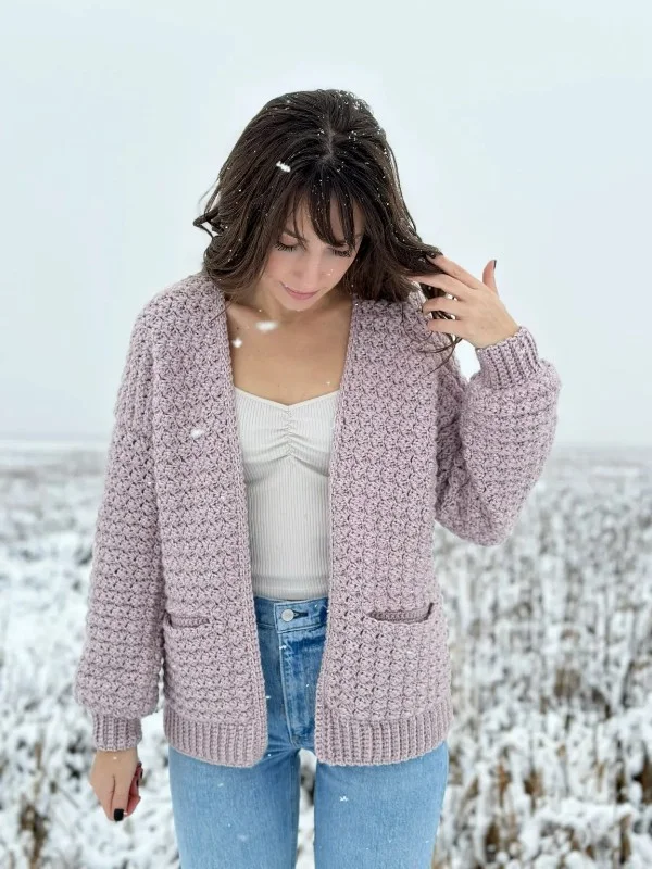 A woman in th esnow weraing a pink crochet cardigan with pockets.