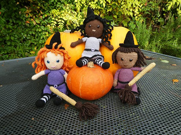Three crochet witch dolls posing with broomsticks and a pumpkin.