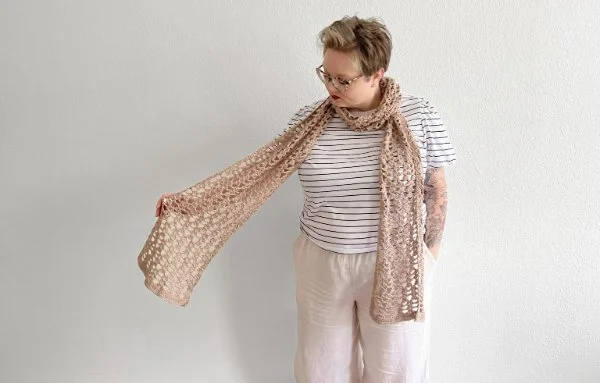 A woman wearing a long, beige coloured, lacy crochet scarf.