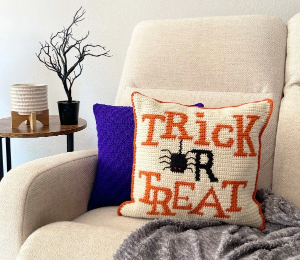 A Trick or treat crochet pillow on a couch.