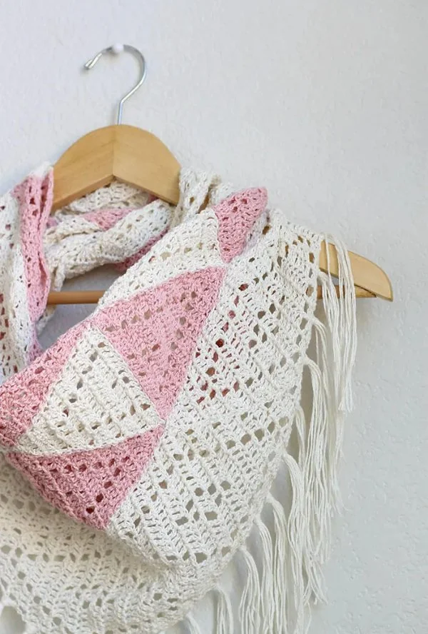 A lacy crochet scarf with pink triangles on a wooden coat hanger.