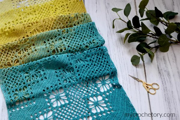 A lacy crochet scarf made in blue and yellow cake yarn.