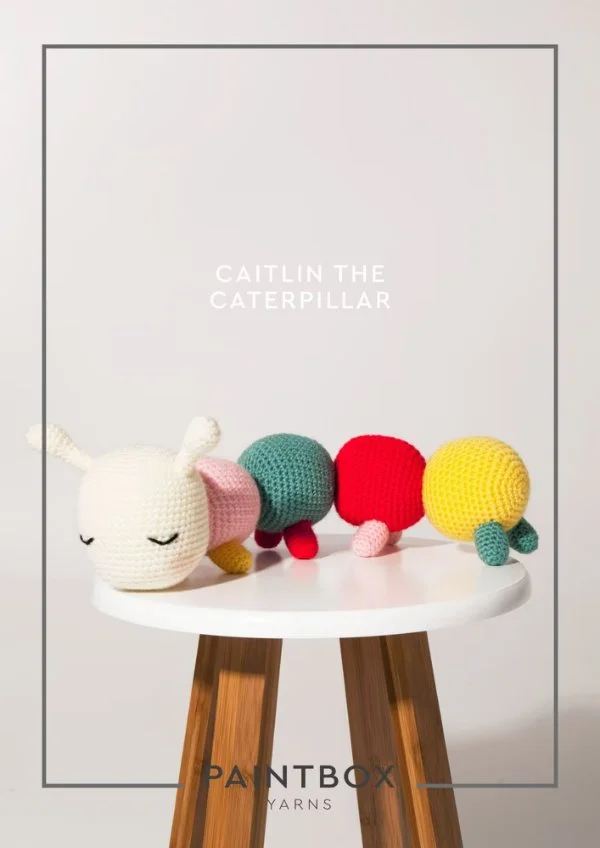 A rainbow crochet caterpilar on a stool.
