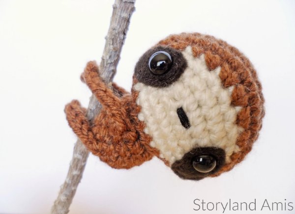 A crochet baby sloth hanging from a twig.