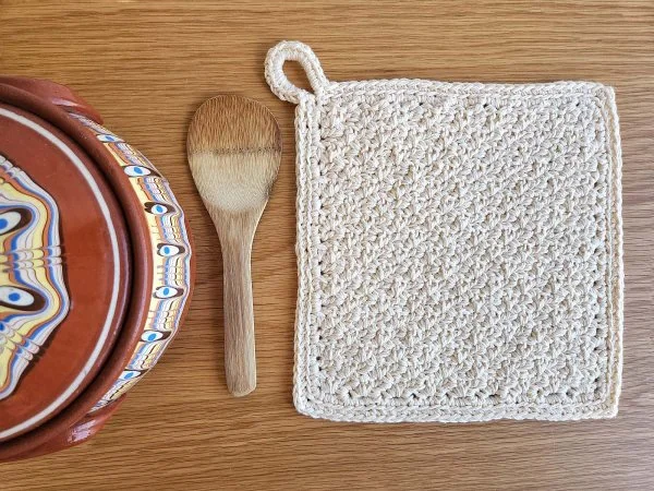 A textured crochet trivet and a wooden spoon.