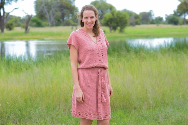 A woman wering a pink, loose-fittin gcrochet dress with a tie belt.