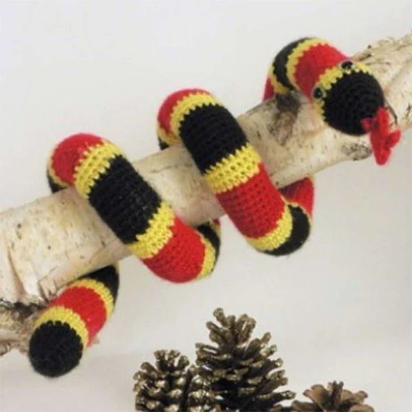 A crochet coral snake coiled around a branch.