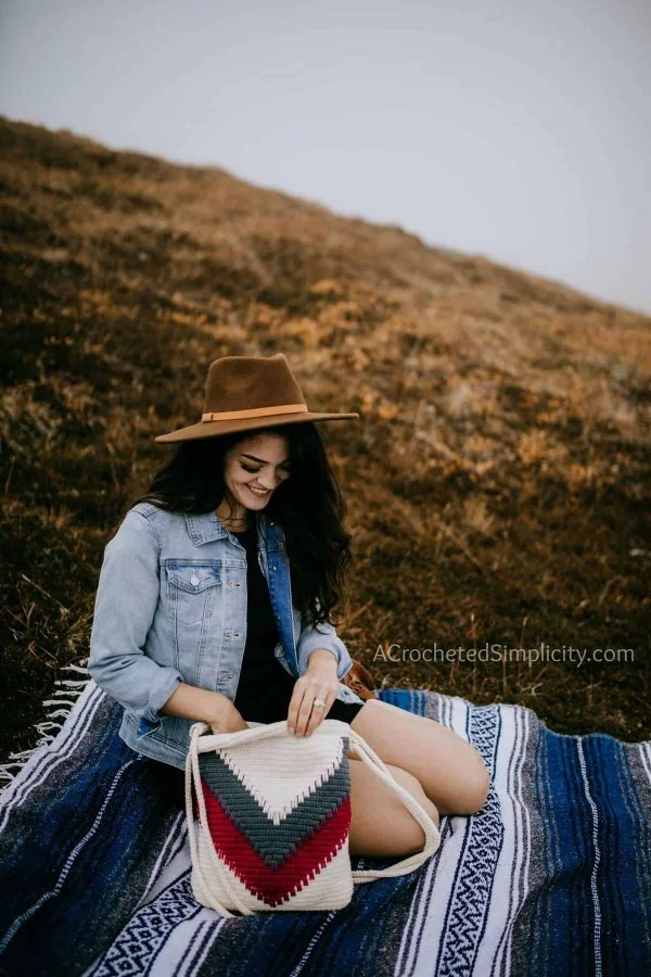 A woman sitting on a hill with a crochet backpack with a chevron design.