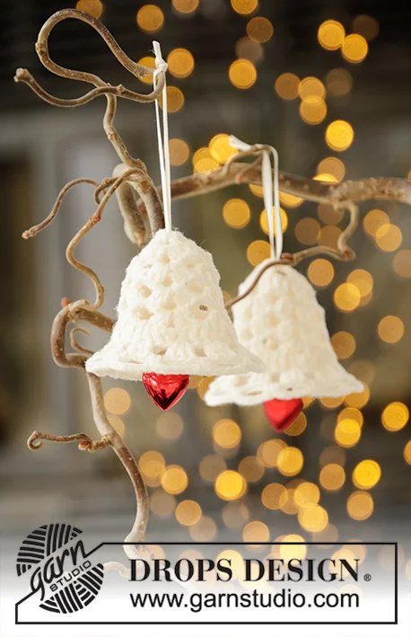 Two white lacy crochet bells with red ringers hanging from a Christmas tree.