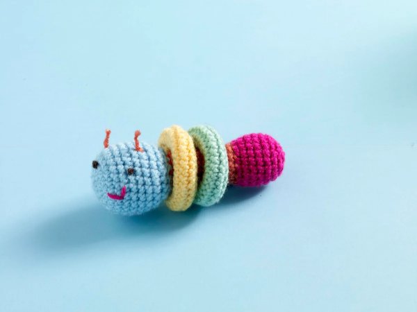 An amigurumi crochet caterpillar baby toy on a blue background.