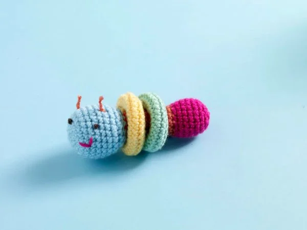 An amigurumi crochet caterpillar baby toy on a blue background.