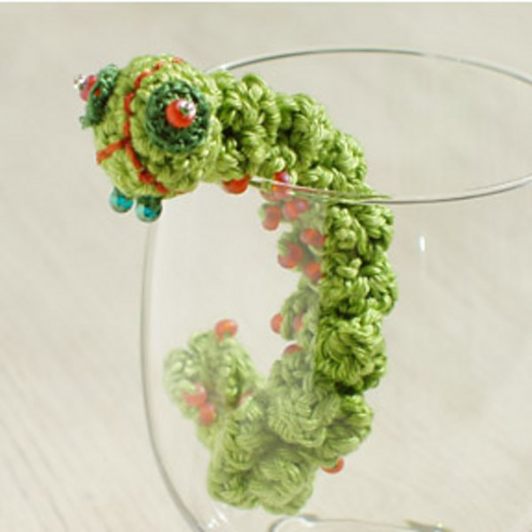 A knobbly green crochet caterpillar climbing up a glass.