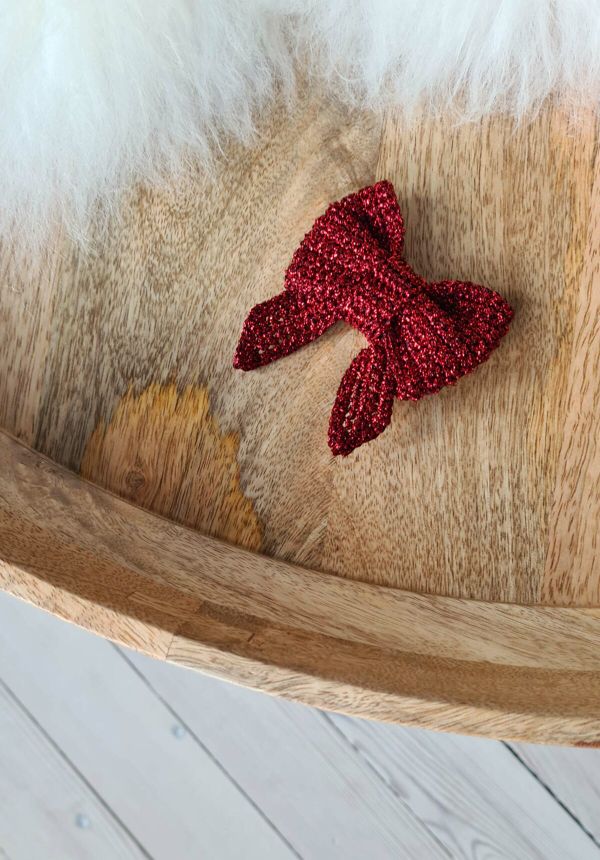 A shiny red crochet Christmas bow ornament in a wooden bowl.