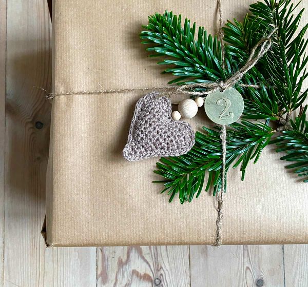 A crochet heart Christmas ornament on a brown paper wrapped Christmas gift.