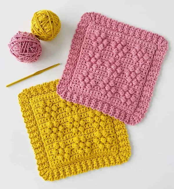 Two brightly coloured crochet hot pads with bobble stitch daisy motifs.