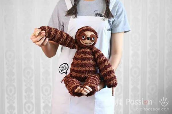 A stripey crochet sloth toy with long arms and legs.