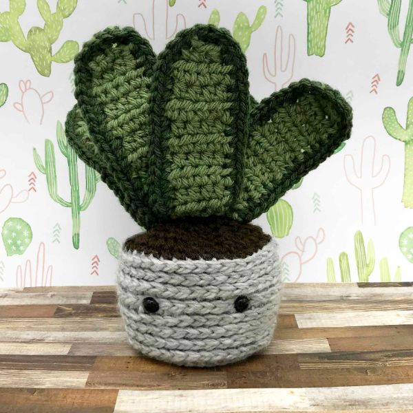 A crochet snake plant in a crochet plant pot with cute little facial features.