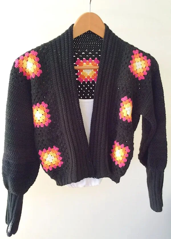 A black crochet Granny Square cardigan on a wooden hanger.