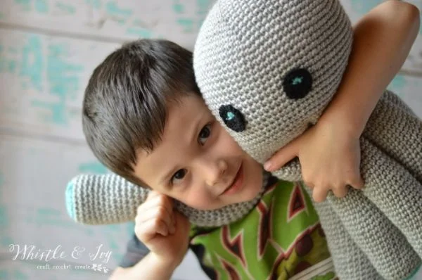 A child hugging a large grey crochet octopus toy.