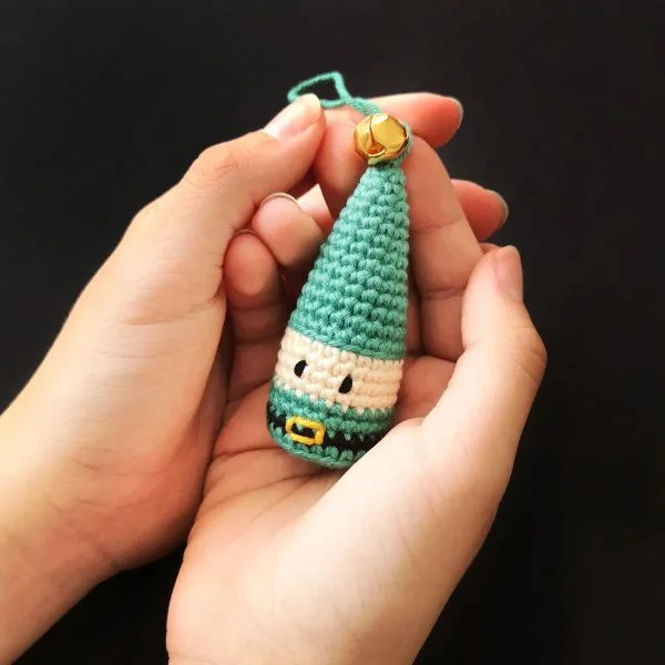 A oerwon holding a small green crochet elf ornament in their hands,