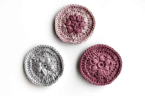 Three crochet flower face scrubbies in pinks and grey.