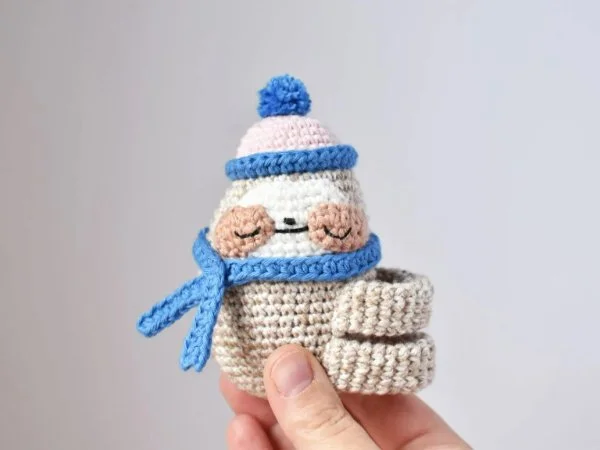 A tiny crochet sloth with a beanie and scarf.