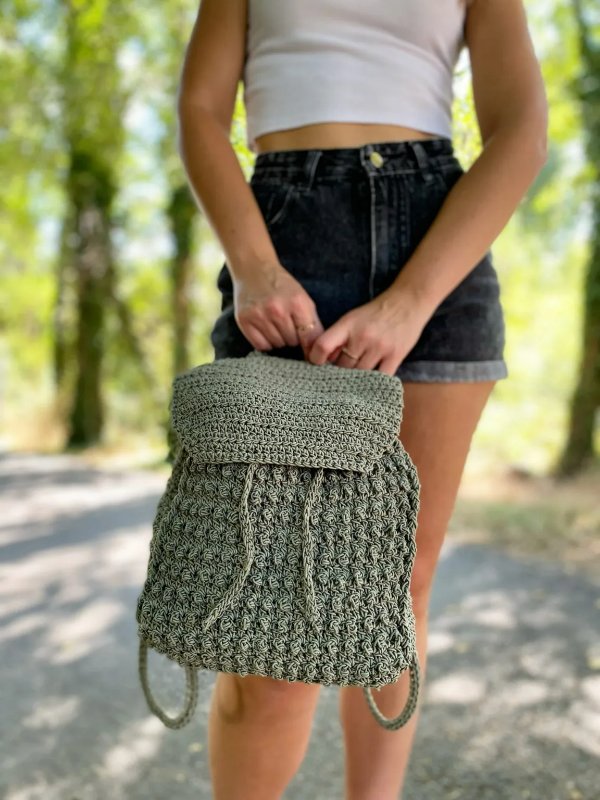 A woman holding a grey-green crochet backpack.