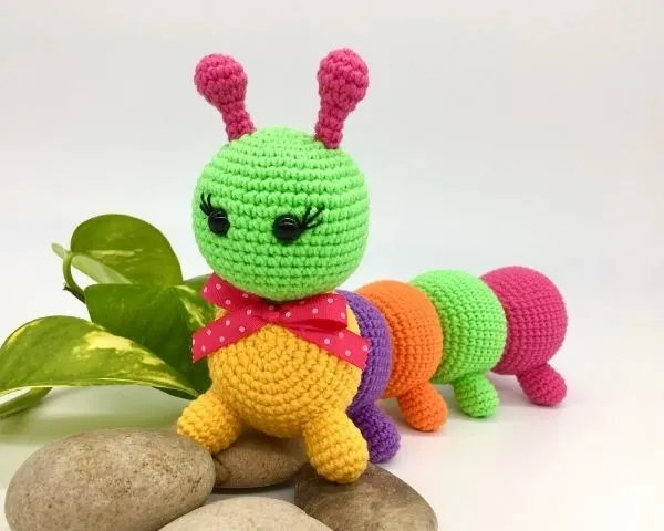 A brightly coloured crochet caterpillar toy with a bow.
